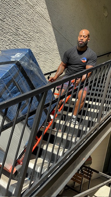 Jabari Andrews carrying a wrapped item up an exterior staircase